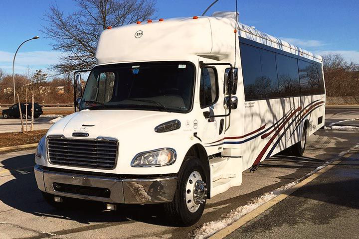 A white Freightliner shuttle bus parked in an outdoor lot on a sunny day.