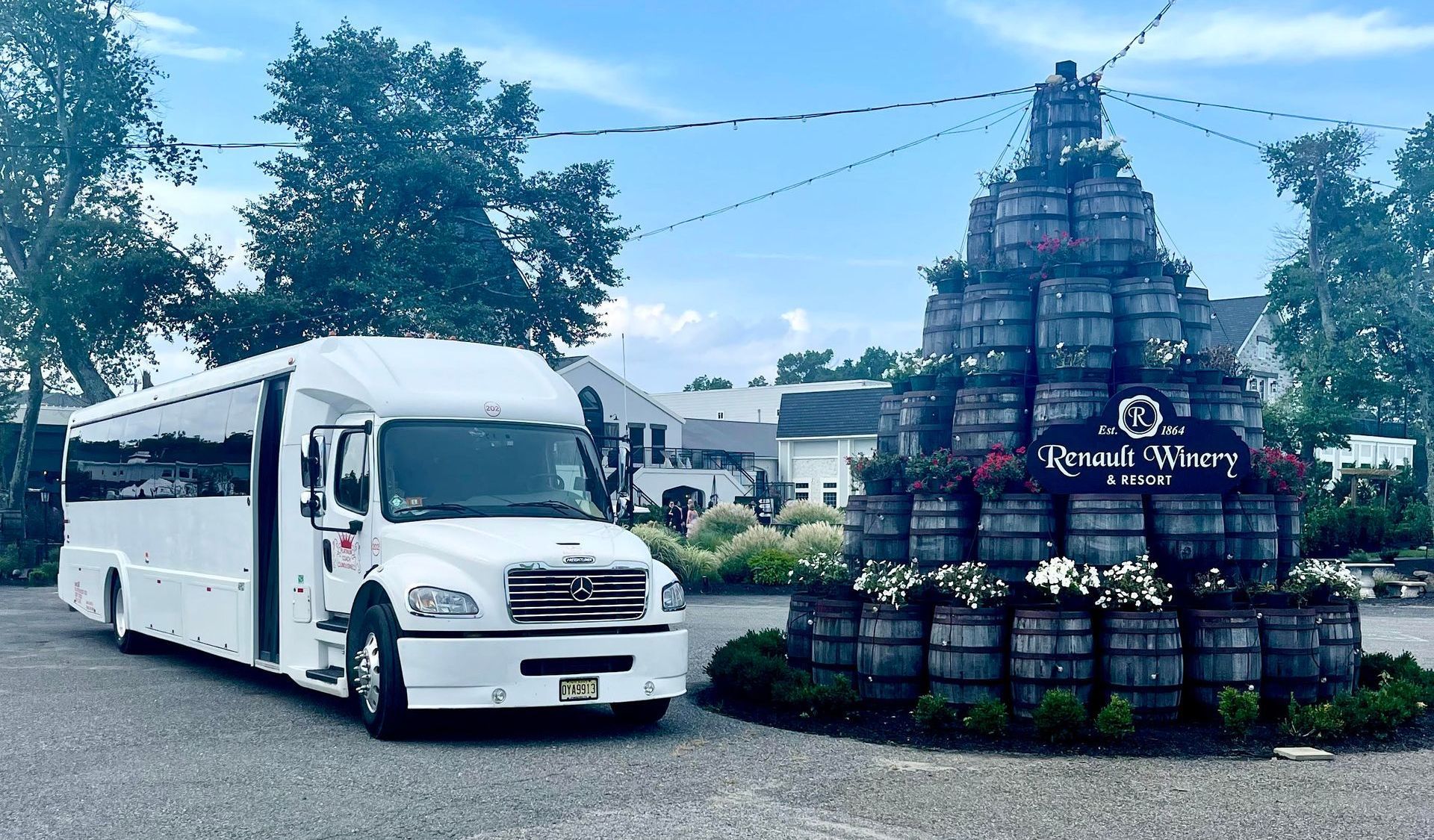 A white bus is parked in front of a stack of barrels.