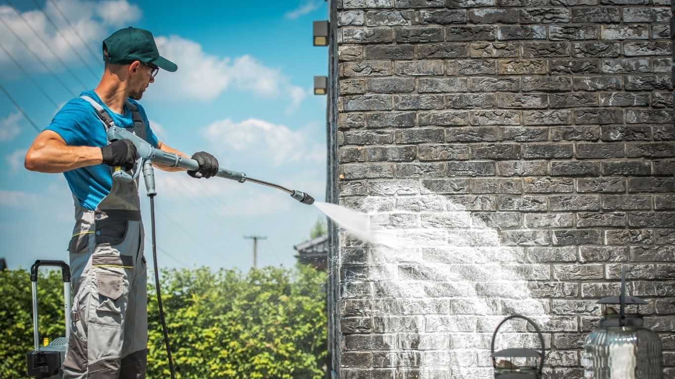 Noble Washing LLC | A man is cleaning a brick wall with a high pressure washer.