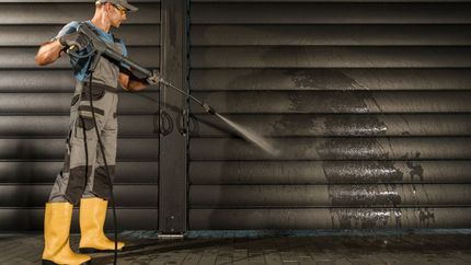 Noble Washing LLC | A man is using a high pressure washer to clean a garage door.