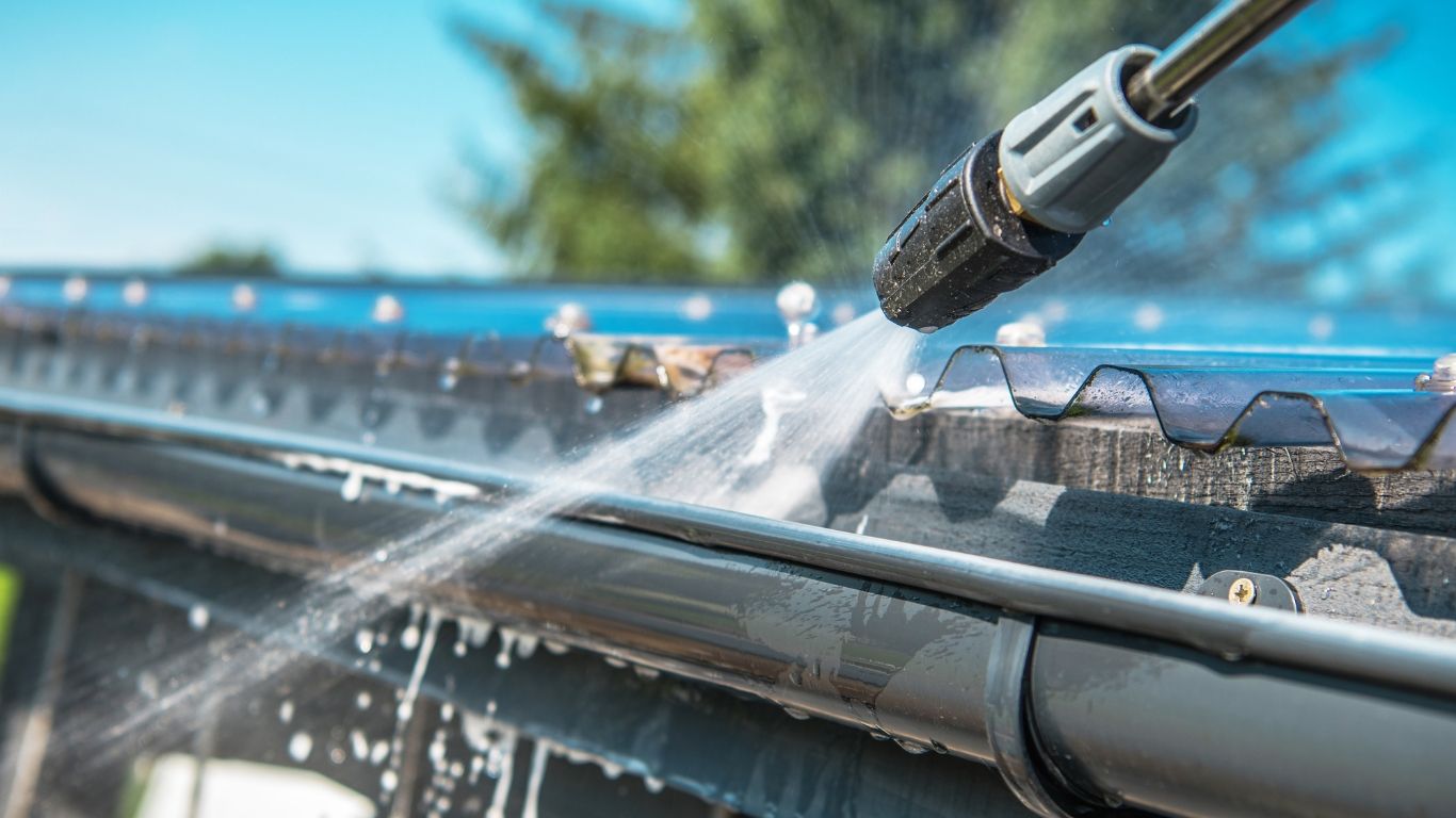 Noble Washing LLC | A person is cleaning a gutter with a high pressure washer.