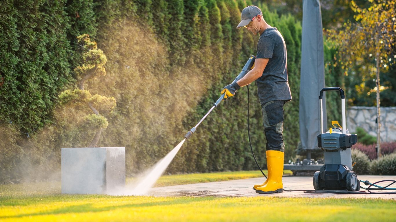 Noble Washing LLC | A man is using a high pressure washer to clean a concrete block.