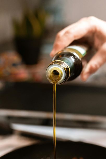 A person is pouring olive oil into a frying pan.