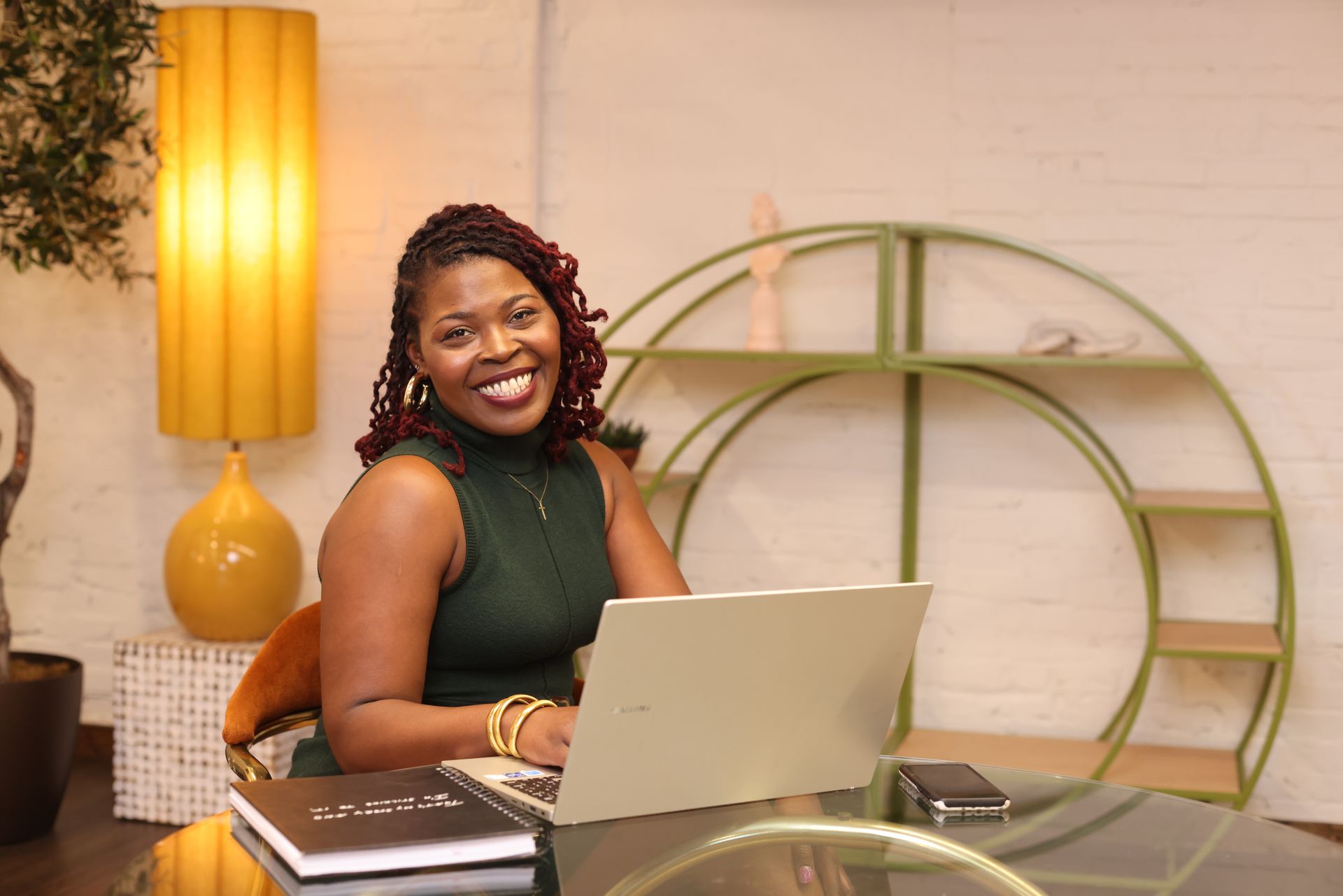 A woman is sitting at a desk with a laptop and a vase of flowers.