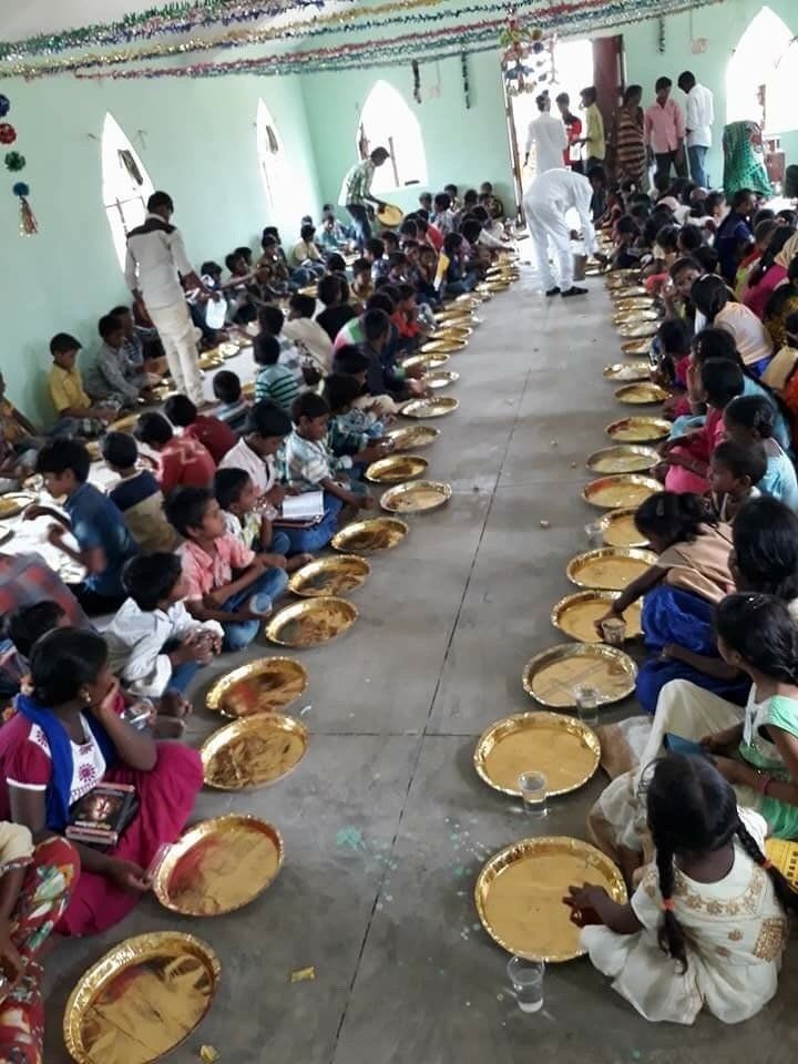 A large group of people are sitting on the floor eating plates of food.