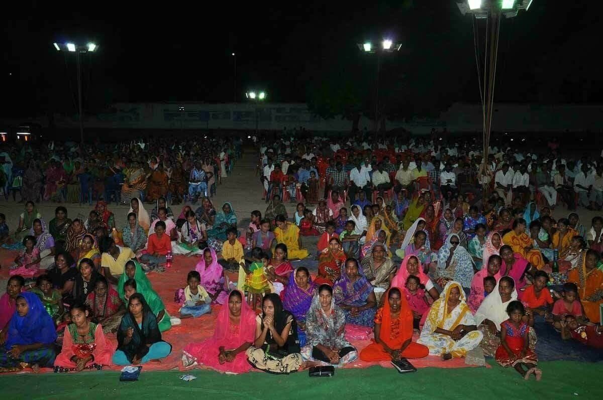 A large group of people are sitting on the ground in a field at night.
