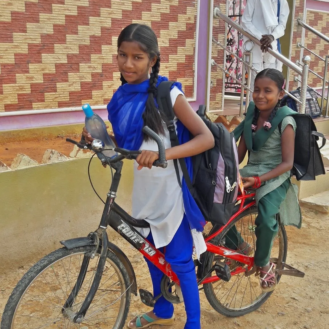 A girl is riding a bike with another girl on the back