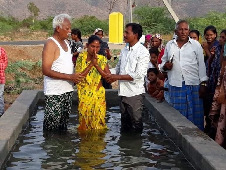 A woman in a yellow dress is being baptised in a pool of water