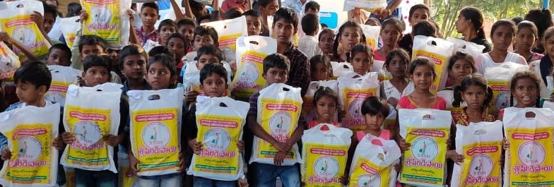 A large group of children are standing next to each other holding bags.
