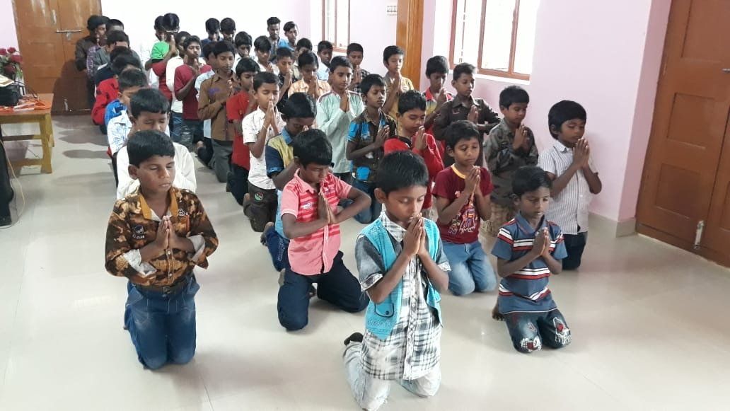 A group of children are kneeling down in a room and praying.