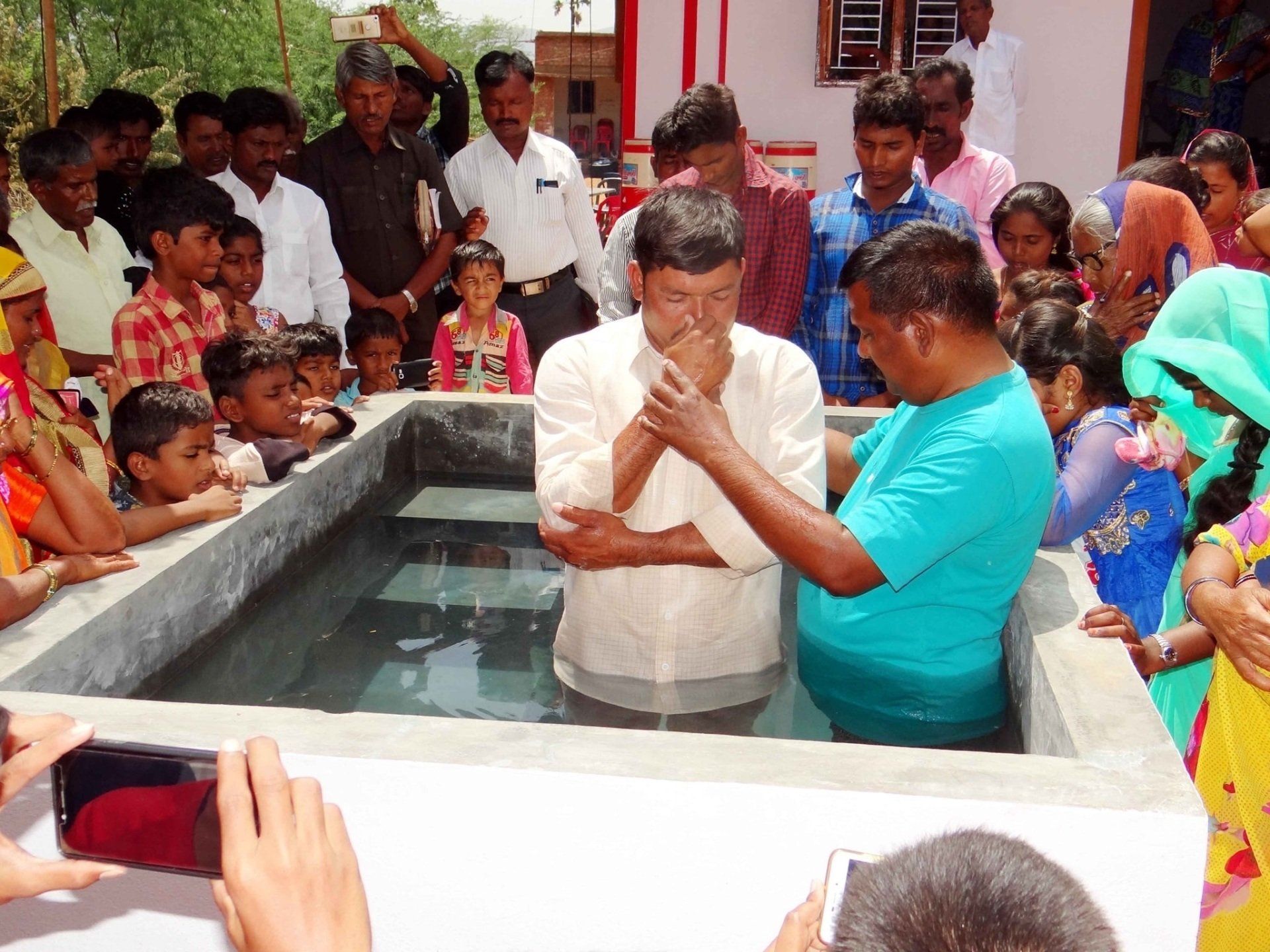 A group of people are gathered around a man being baptised