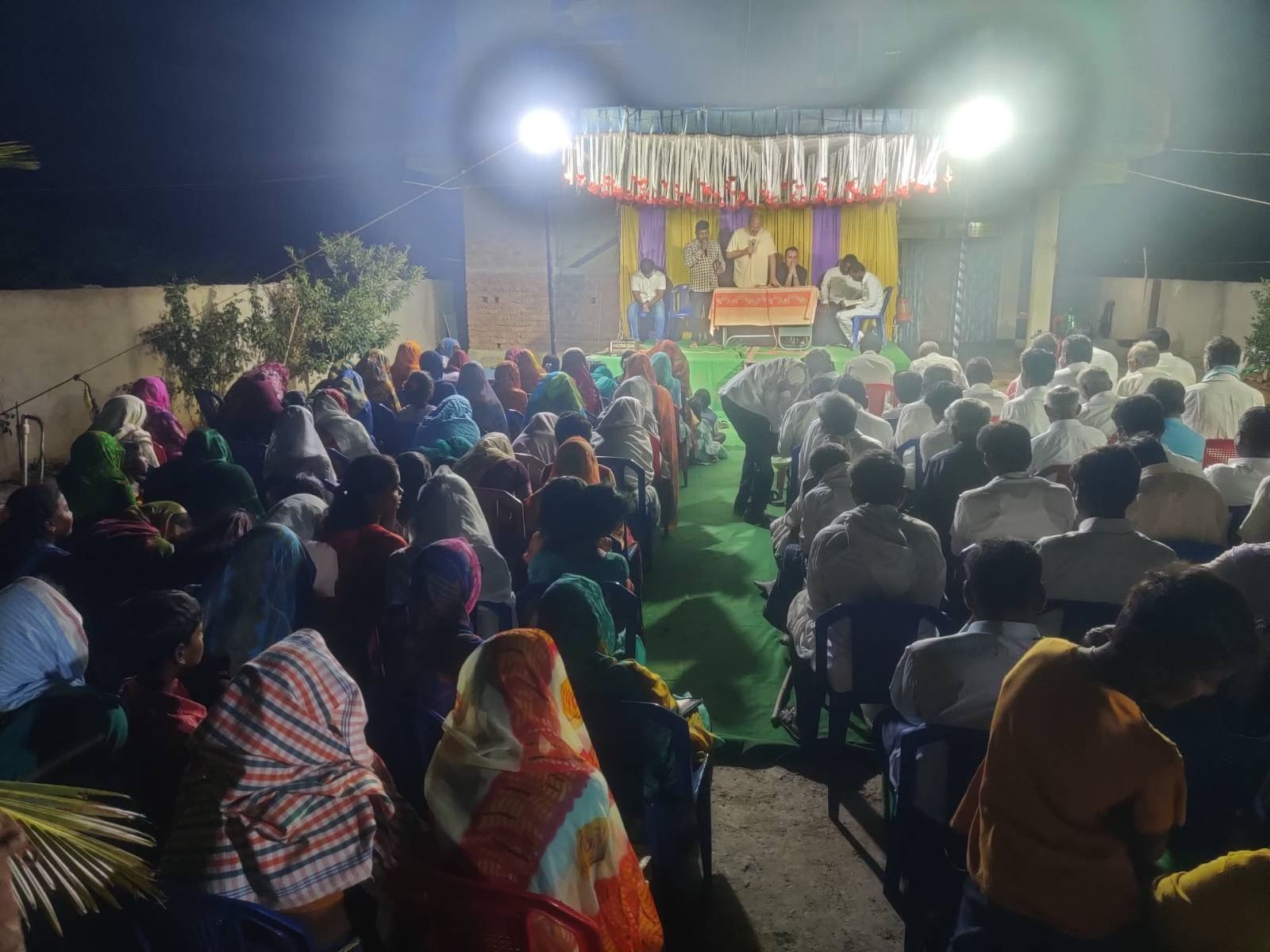 A large group of people are sitting in front of a stage at night.