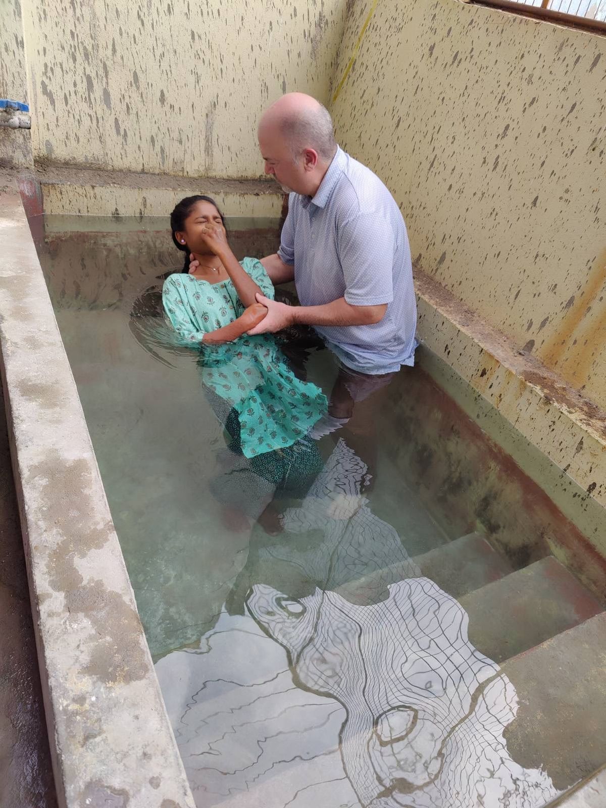 A man is baptizing a woman in a pool of water.
