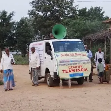 A white van with a green horn on top of it is parked in a dirt field.