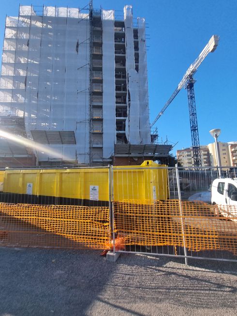 Cantiere con impalcature che avvolgono un edificio; gru rossa sullo sfondo; striscione con la scritta