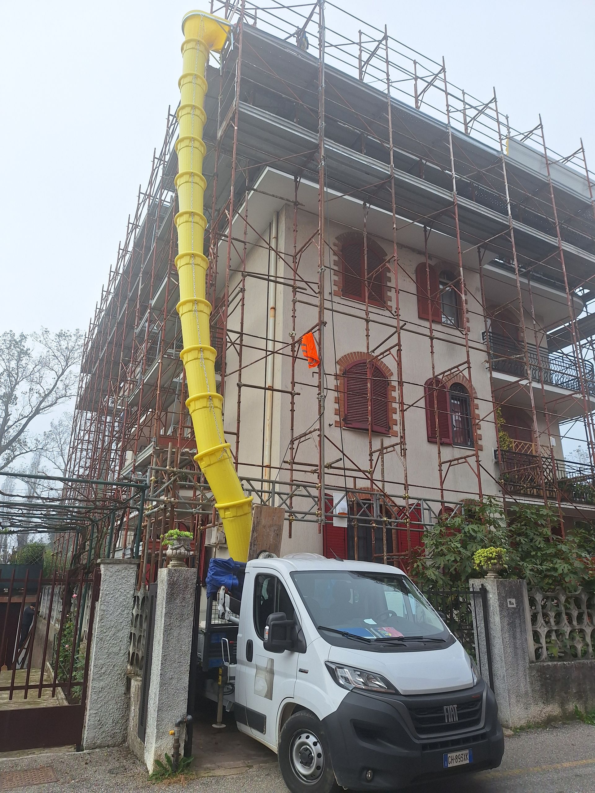 Camion bianco con scivolo giallo per detriti contro una casa sotto un'impalcatura.