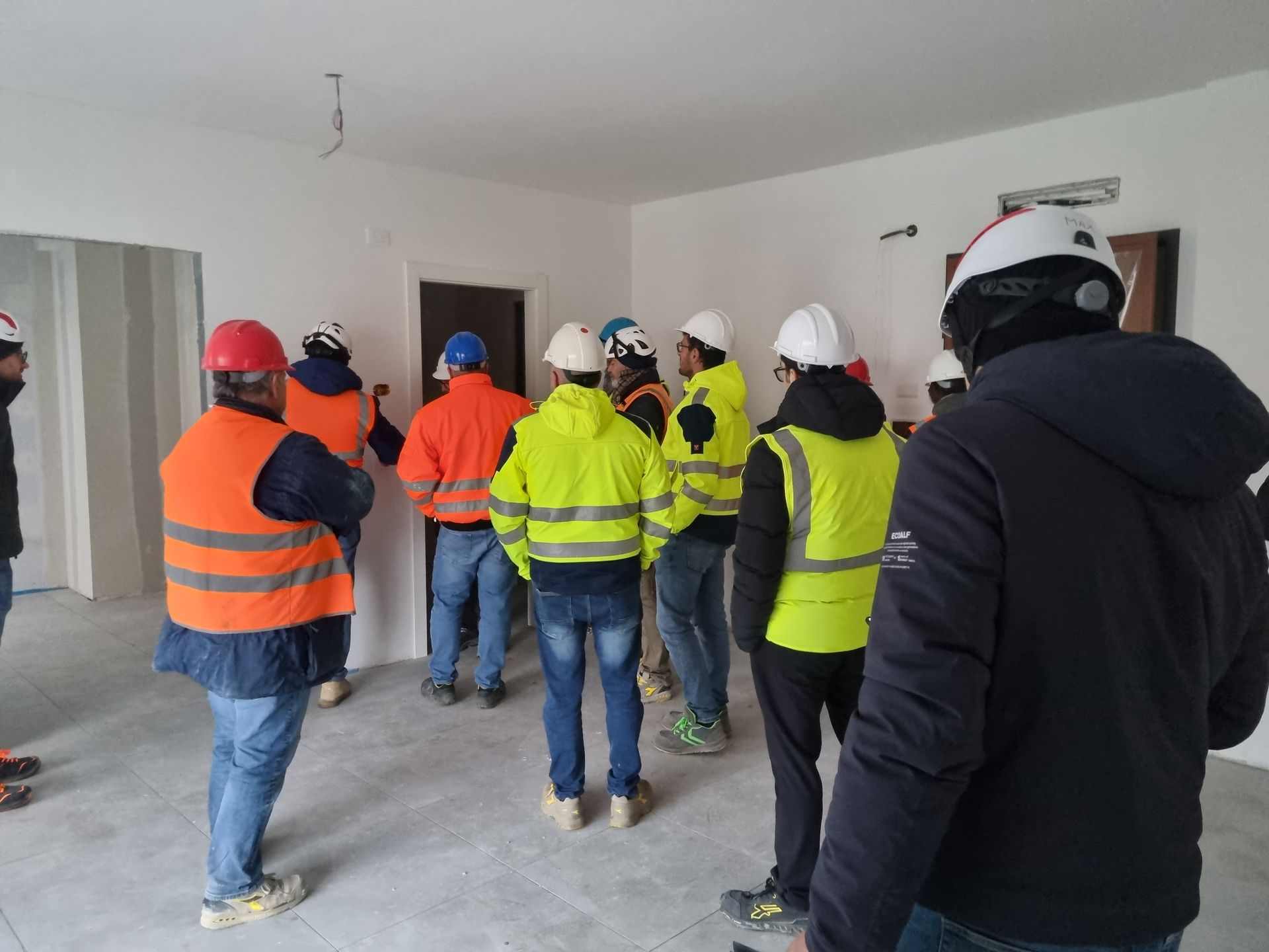 Gli operai edili, in tuta di sicurezza, si sono radunati in una stanza, probabilmente un cantiere.