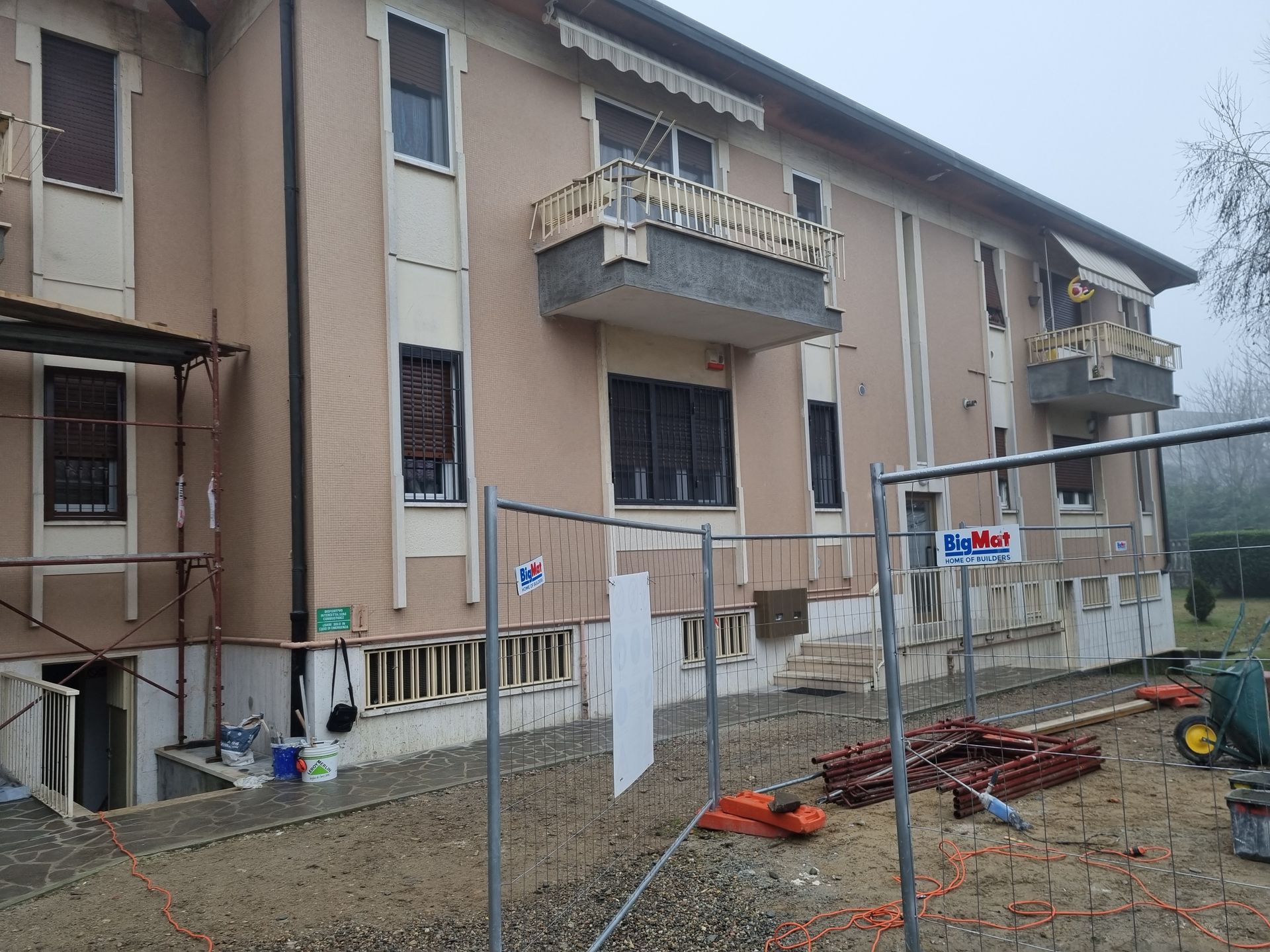 Edificio in costruzione con impalcature e recinzione; facciata beige, balconi.