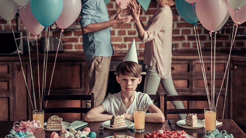 Unhappy child at a birthday party with parents arguing in background