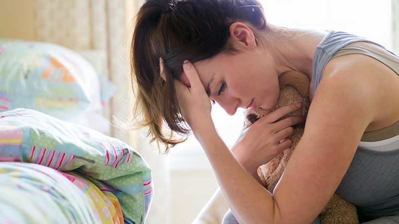 Woman holding teddy bear and looking distraught