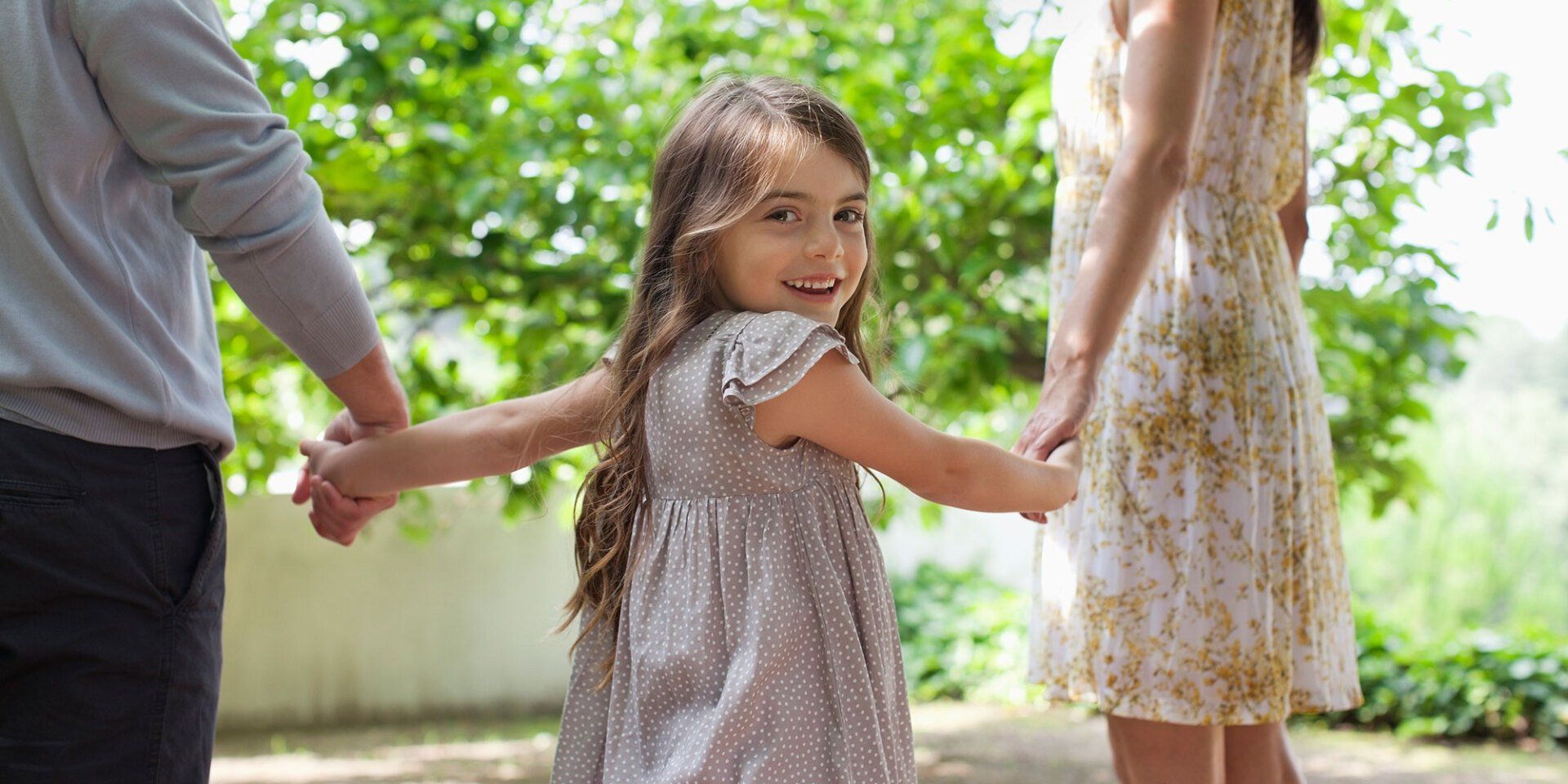 young girl holding hands with two adults