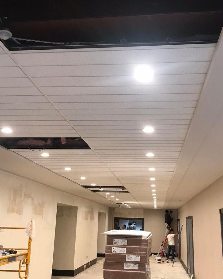 A man is standing on a ladder in a room with a ceiling that is being remodeled.