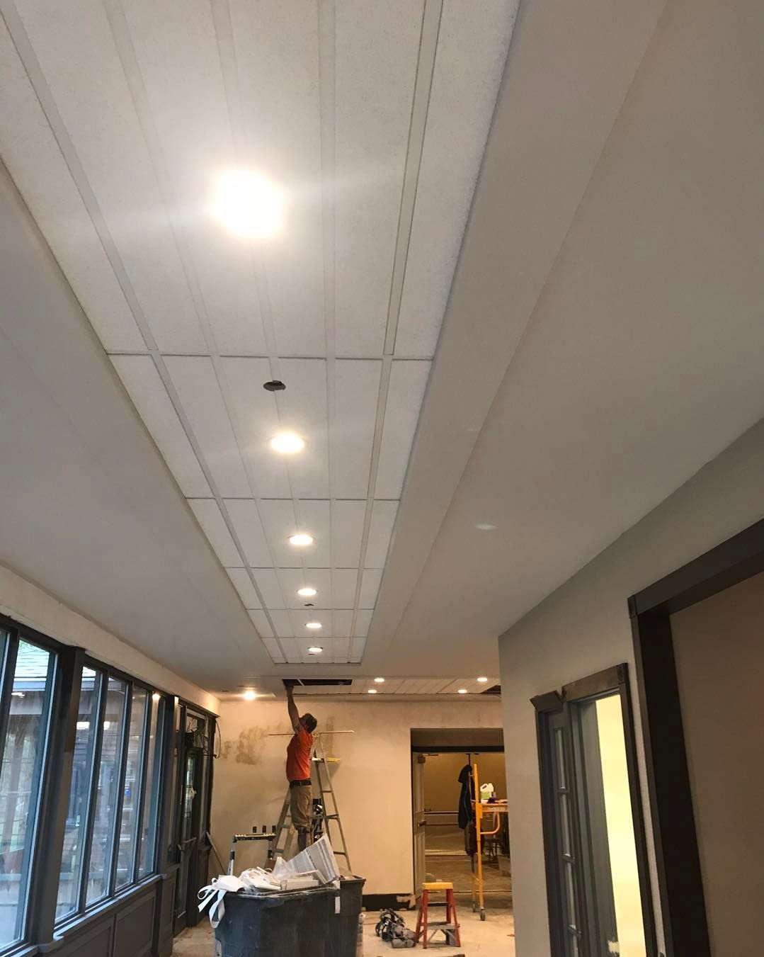 A man is standing on a ladder working on the ceiling of a building.