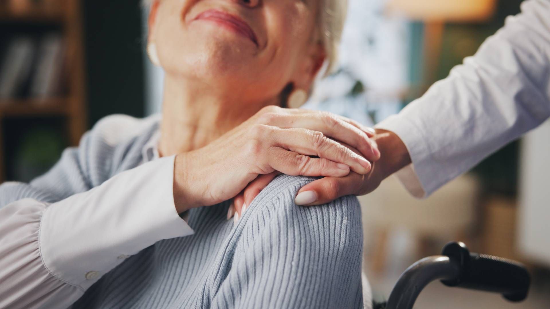 Person in a wheelchair with a hand on their shoulder, receiving support. Indoor setting.