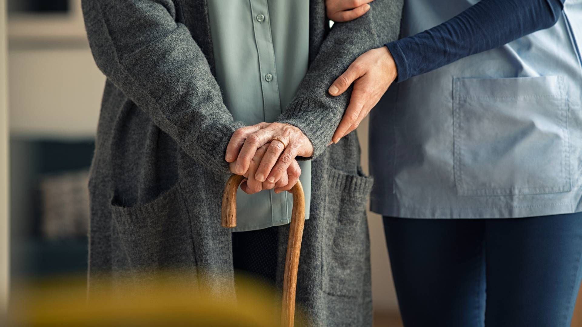 Person holding a cane is assisted by another person, indoors.