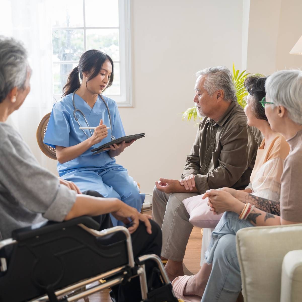 Nurse in blue scrubs reviews tablet with group of seniors indoors.