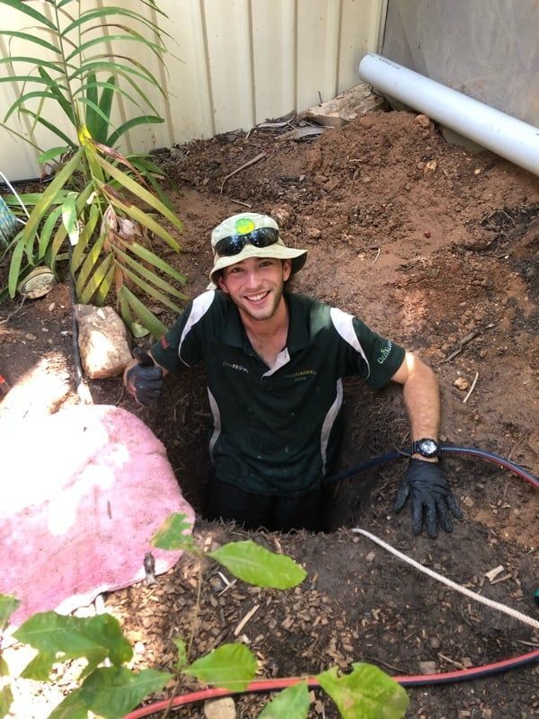 A Man in a Hat is Standing in a Hole in the Ground — Wigg Plumbing in Berrimah, NT