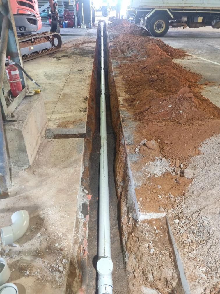 A Trench With White Pvc Pipes Installed Inside A Workshop, With A Cement Floor And Dirt — Wigg Plumbing in Berrimah, NT