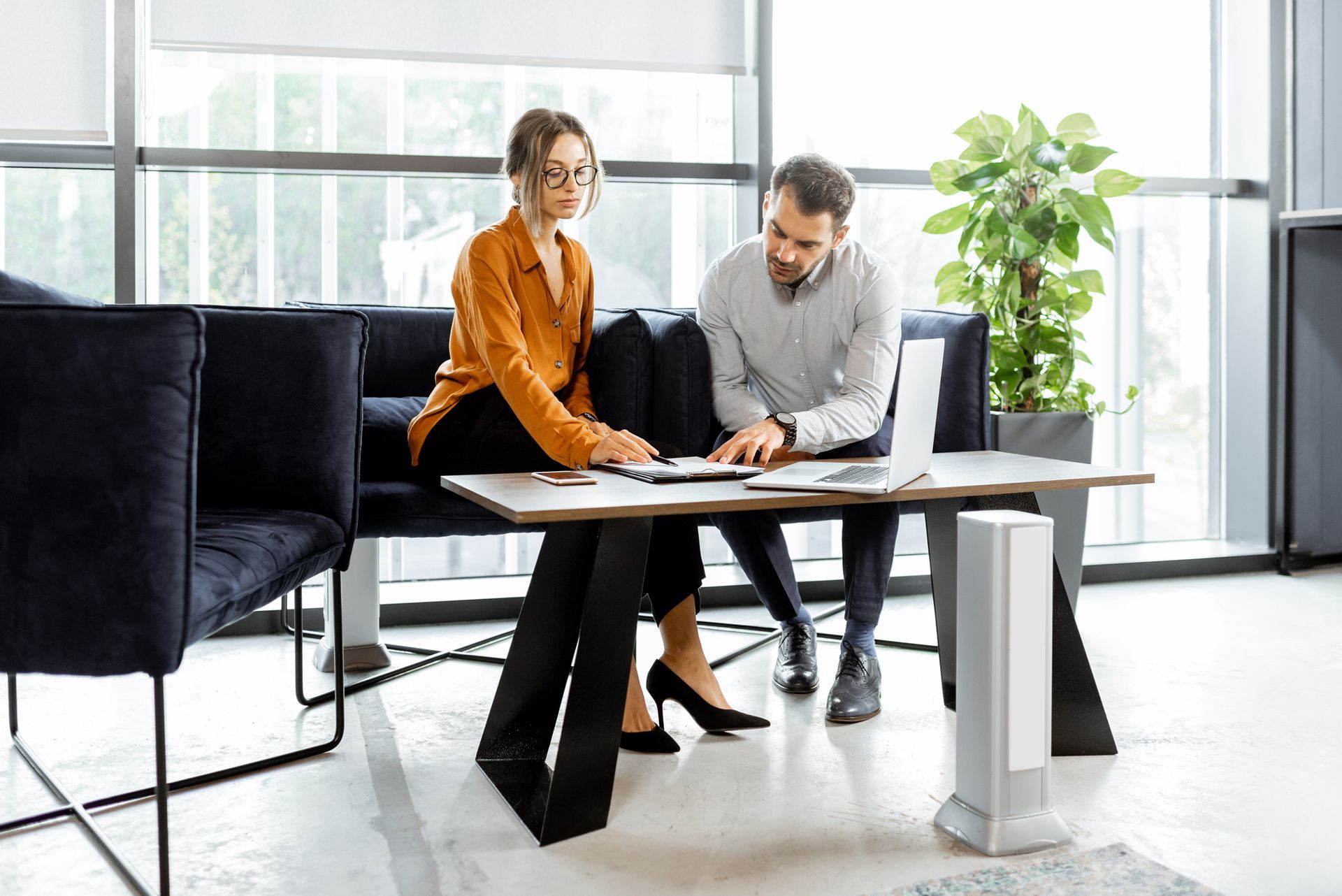 A man and a woman are sitting at a table looking at a laptop.