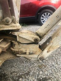 A close up of a piece of wood sitting on top of a gravel road next to a red car.