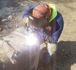 A man wearing a welding helmet is welding a pipe.