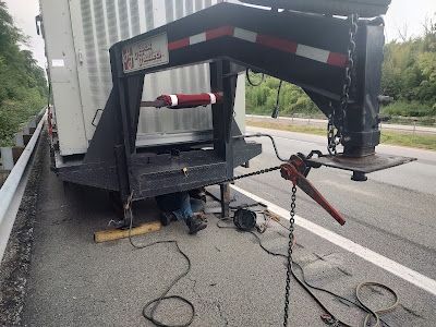 A man is working under a trailer on the side of the road.