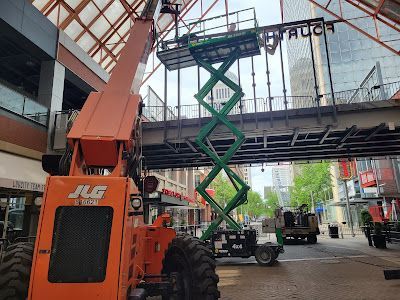 A scissor lift is sitting under a bridge in a city.