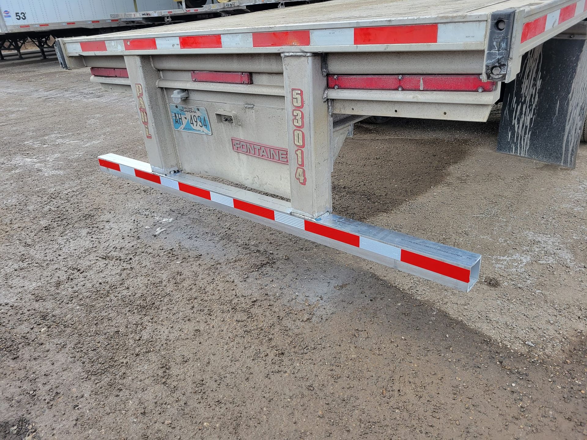A trailer with a red and white stripe on the back is parked on a dirt road.