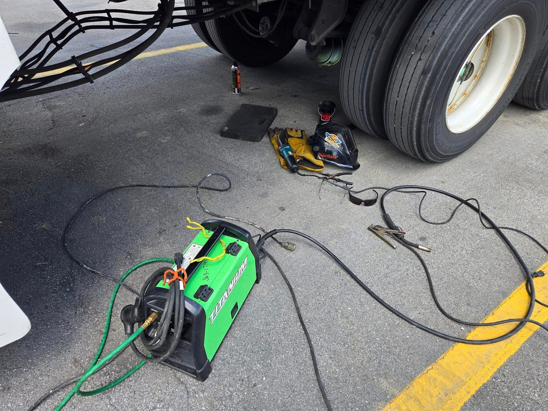 A green welding machine is sitting under a truck in a parking lot