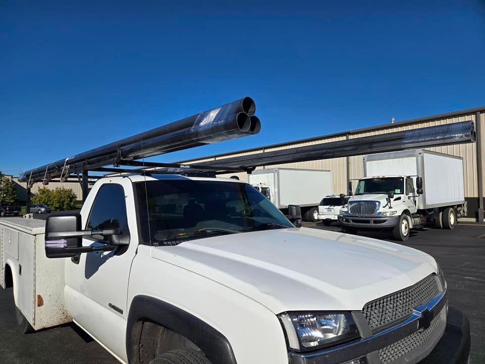 A white truck with pipes on top of it is parked in front of a building.