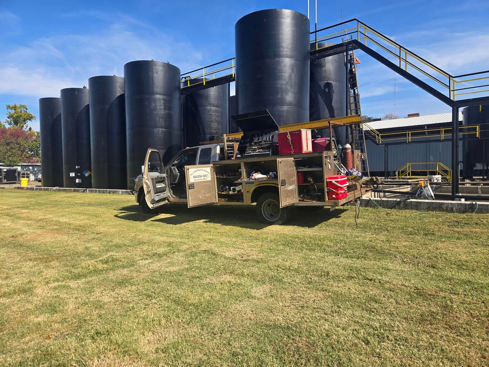 A truck is parked in front of a row of large black tanks.