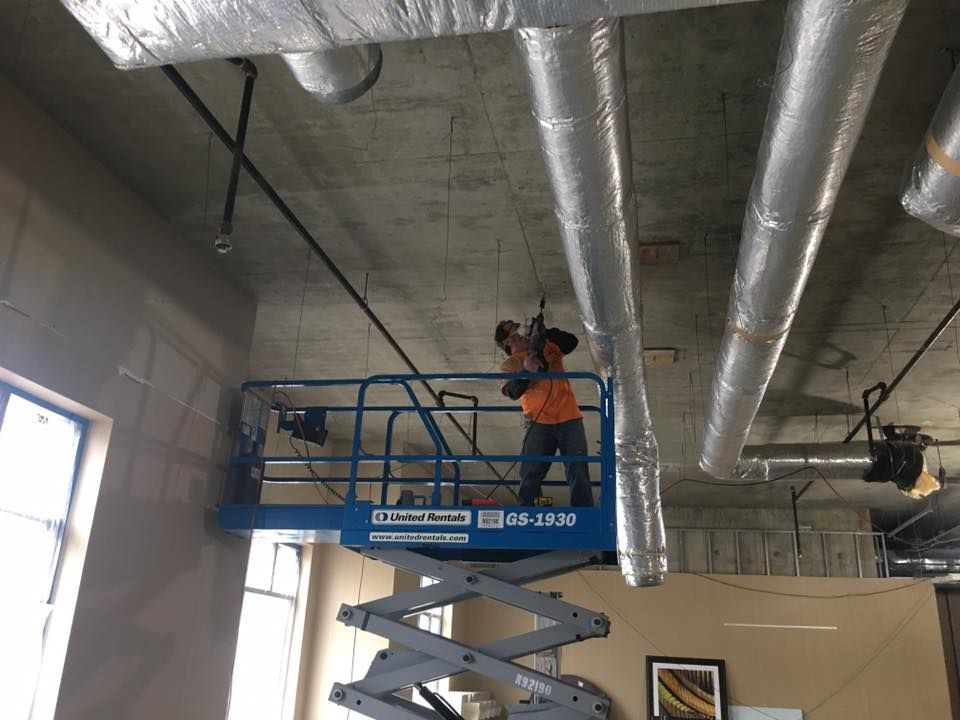 A man is standing on a scissor lift working on a ceiling.