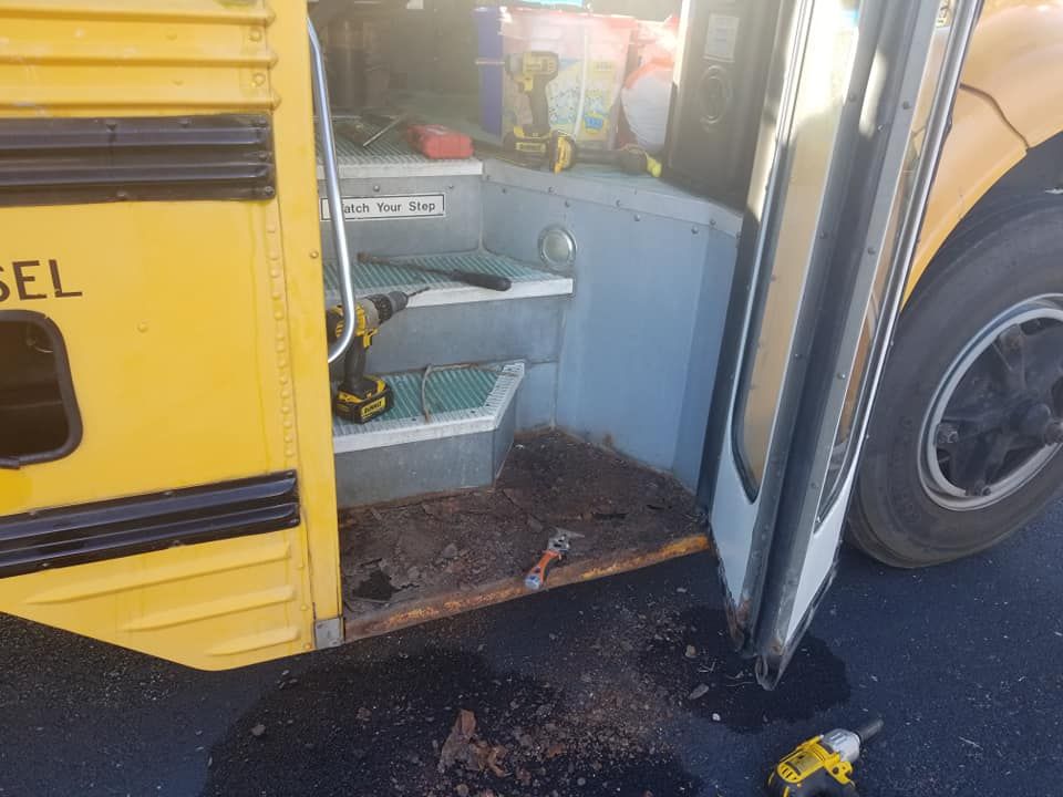 A yellow school bus with the door open and a drill in the doorway.