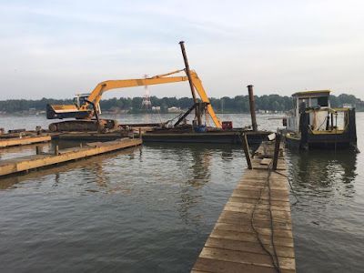 A large yellow excavator is sitting on top of a large body of water next to a dock.