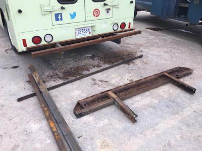 A white bus is parked in a parking lot next to a piece of metal.