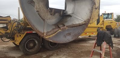 A yellow concrete mixer truck is parked in a dirt lot next to a ladder.