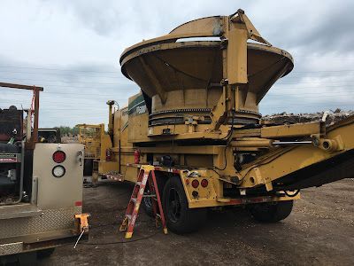 A large yellow machine is parked in a dirt lot next to a ladder.