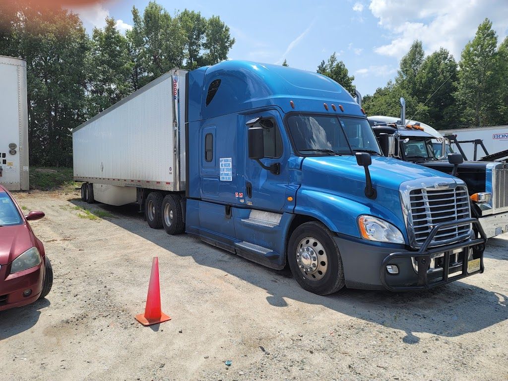 A blue semi truck with a white trailer is parked in a gravel lot.
