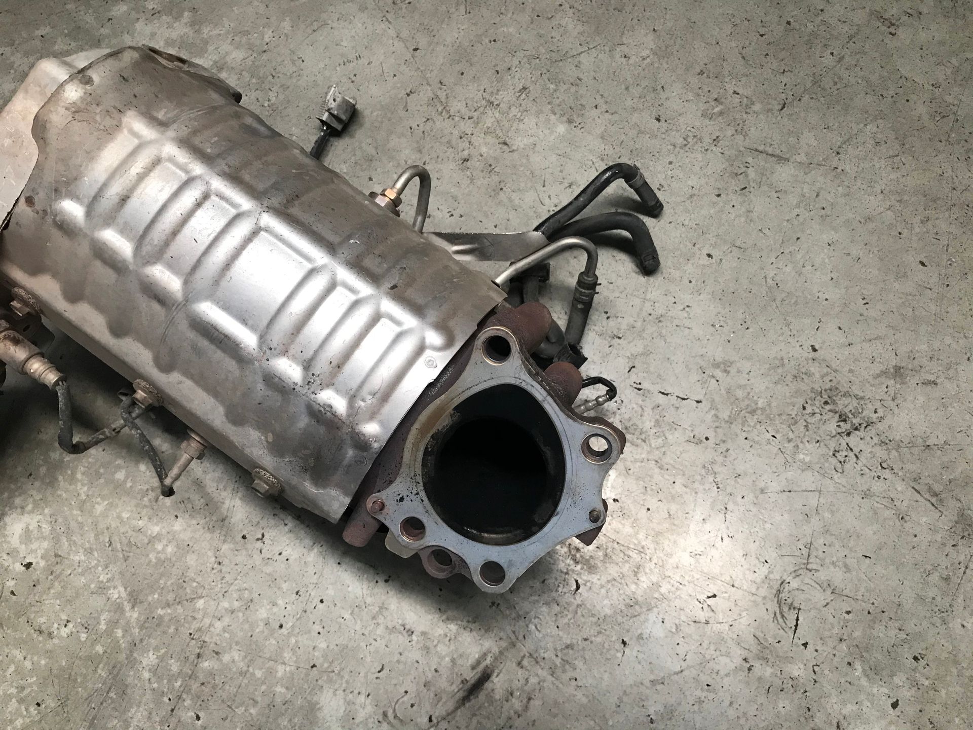 Catalytic converter with sensors and mounting flange on a concrete surface.