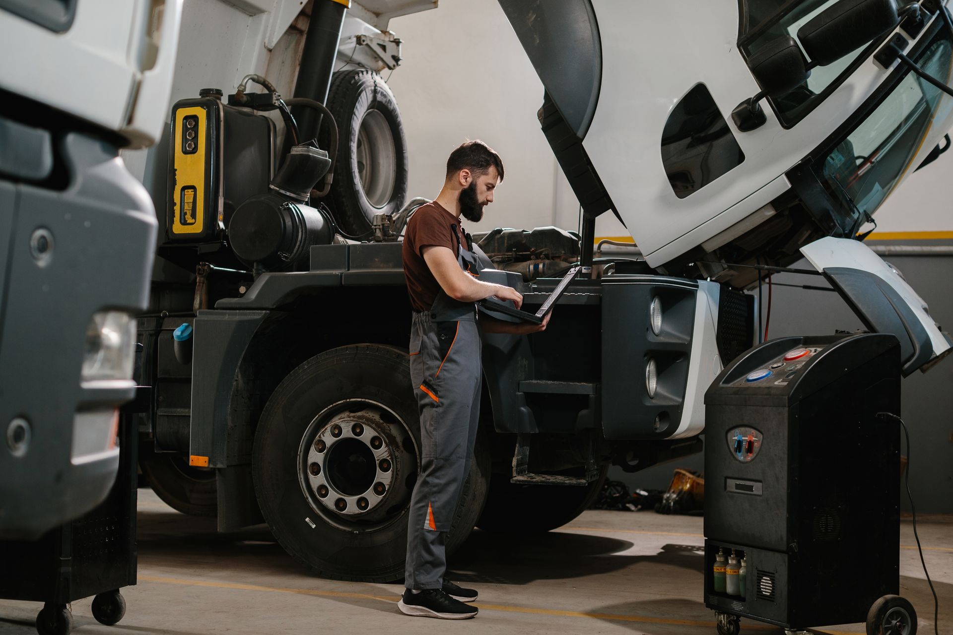 Mechanic using laptop to diagnose truck engine with hood open, in a garage.